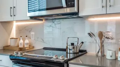 A close-up of a stylish kitchen with a stainless steel stove, microwave, and a marble backsplash.