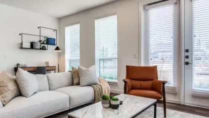 A cozy living room with a light gray couch, a brown leather chair, and a marble coffee table.