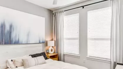 A serene bedroom with a white bed, soft gray accents, and an abstract blue painting above the headboard.