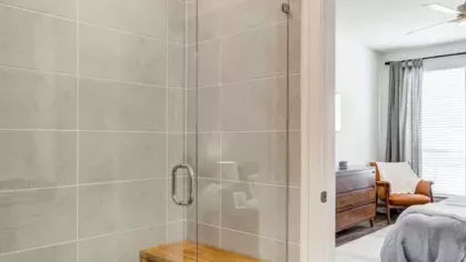 A walk-in shower with large beige tiles, a glass door, and a built-in wooden bench.