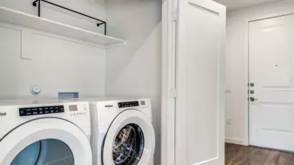 A compact laundry area featuring a stacked Whirlpool washer and dryer tucked behind folding doors.