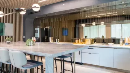 A stylish communal kitchen with a long marble dining table, high chairs, and elegant pendant lighting.