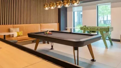 A game room with a shuffleboard table, pool table, foosball, and modern pendant lighting.