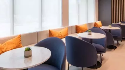 A café-style seating area with blue chairs, round marble tables, and plush accent pillows along the bench seating.