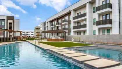 A resort-style pool surrounded by modern apartment buildings, featuring a walking path over the water.