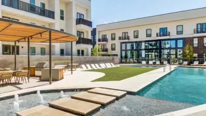 A poolside lounge area with a shaded grilling station, sun loungers, and a tranquil water feature.