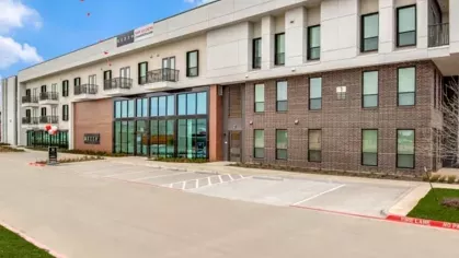 The exterior of a contemporary apartment building with large windows, a brick and white facade, and a leasing center entrance.