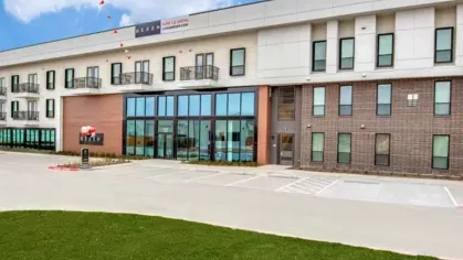 A wide-angle view of the apartment complex exterior, showcasing its modern architecture, green landscaping, and bright blue skies.