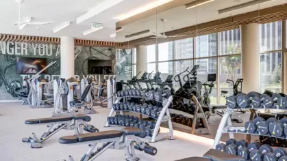 A spacious gym area with rows of free weights, weight benches, and a mirrored wall.