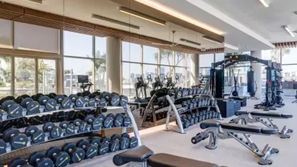 A gym with an extensive range of dumbbells, weight benches, and large windows for natural light.