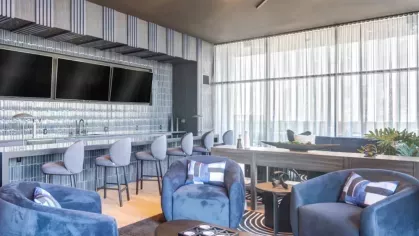 Sleek lounge with blue velvet chairs, a bar, and a modern ceiling design.
