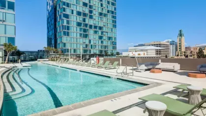 Modern pool surrounded by green lounge chairs, two tall glass buildings, and a clear blue sky in an urban setting.