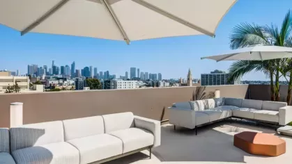 Shaded rooftop lounge with white sofas, geometric orange tables, and expansive city views.
