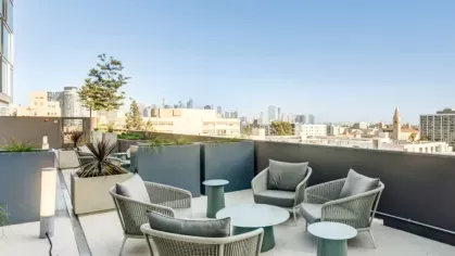 Cozy outdoor seating with gray woven chairs and small tables on a rooftop terrace with city views.