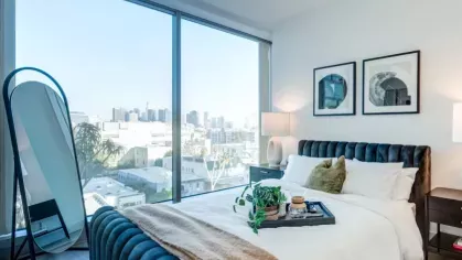 Bedroom with a plush blue headboard, modern decor, and expansive window with city views.