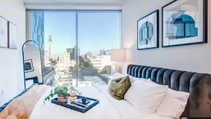 Bedroom featuring a soft bed, modern artwork, and a large window with an urban landscape.