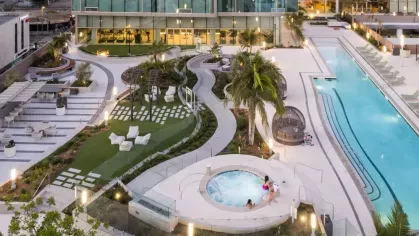 Aerial view of Nari's rooftop amenities including a pool, hot tub, green spaces, and seating areas surrounded by modern glass buildings.