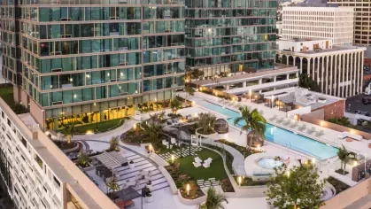 Wide shot of Nari's rooftop showcasing landscaped paths, a long pool, a hot tub, and stylish seating areas against a backdrop of glass towers.