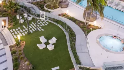 Closer view of the green lawn area with modern white loungers, a hot tub, and the pool at Nari's rooftop amenity deck.