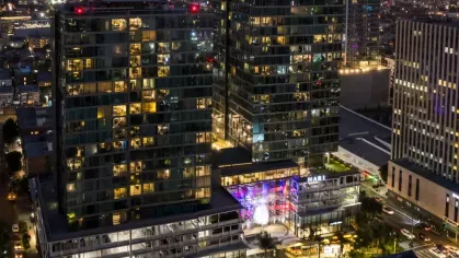 Nighttime aerial shot of the illuminated Nari towers surrounded by the city lights of Koreatown, highlighting the rooftop pool and amenities.