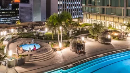 Illuminated rooftop garden at Nari with winding paths, vibrant greenery, and a pool area set against the glowing cityscape.