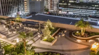 Illuminated rooftop garden and lounge area with city views at sunset.