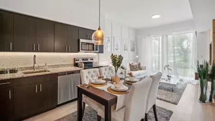 A sleek open-concept kitchen and living space with dark wood cabinetry, stainless steel appliances, and a stylish dining area with elegant pendant lighting.