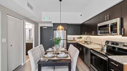 A sophisticated dining nook set against a gourmet kitchen with stainless steel appliances, dark wood cabinetry, and modern pendant lighting.