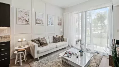 A refined living room with a white sofa, stylish decor, and a coffee table with decorative accents, set against floor-to-ceiling windows with a scenic outdoor view.
