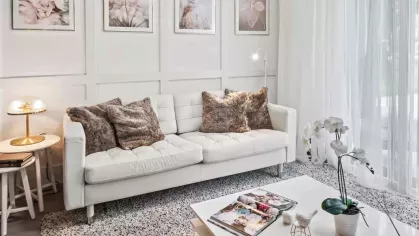 A modern living room with a white tufted sofa, plush fur pillows, and a minimalist coffee table, accented by nature-inspired wall art and warm lighting.