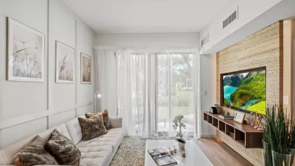 The Oak Enclave apartments offer a modern living space with a mounted TV, floor-to-ceiling windows, and an inviting atmosphere.