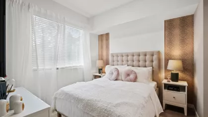 A sophisticated bedroom at Oak Enclave Luxury Apartments, featuring a tufted headboard, soft white bedding, and stylish accent lighting.