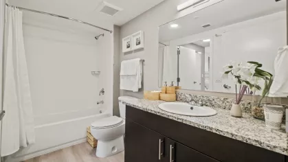 A modern bathroom at Oak Enclave Apartments, featuring a spacious vanity with granite countertops, a large mirror, and contemporary fixtures.