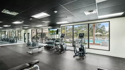 The Oak Enclave luxury apartment gym features state-of-the-art fitness equipment, free weights, and scenic outdoor views of the pool area.