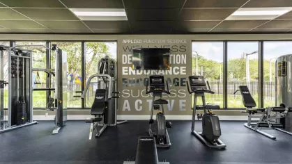 A well-equipped gym featuring treadmills, elliptical machines, and strength training equipment, with large windows showcasing lush outdoor landscaping.