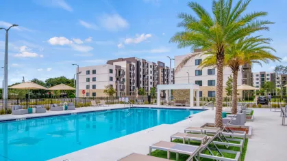 A spacious pool deck with modern lounge chairs and umbrellas, offering a perfect retreat with a backdrop of the upscale apartment buildings.