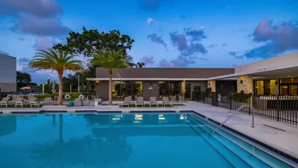 A breathtaking twilight view of the luxury swimming pool, with warm lights from the clubhouse adding to the inviting ambiance.
