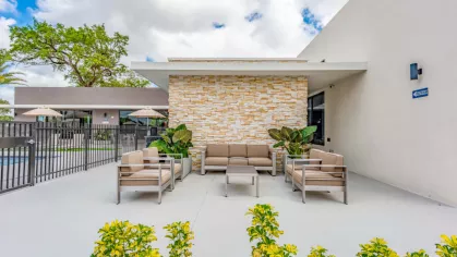 A welcoming outdoor seating area with cushioned chairs and lush greenery, set against a striking stone accent wall at Oak Enclave’s community clubhouse.