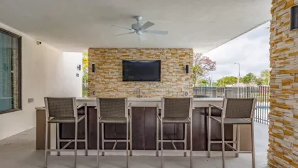 Outdoor bar and entertainment area at Oak Enclave, complete with high-top seating, a built-in TV, and a stone-accented bar for social gatherings.