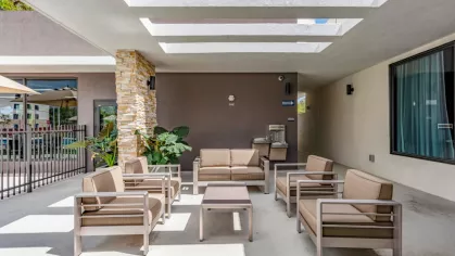 A shaded outdoor lounge at Oak Enclave featuring modern patio seating, stone columns, and a pergola-style roof, creating the perfect setting for relaxation.