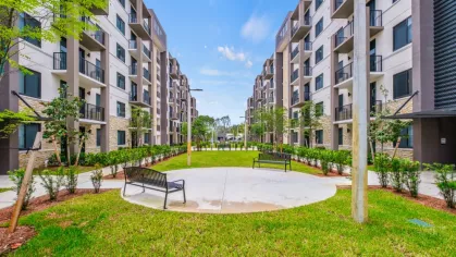 Beautifully landscaped courtyard at Oak Enclave Luxury Apartments, featuring lush green grass, park benches, and modern apartment buildings with private balconies.