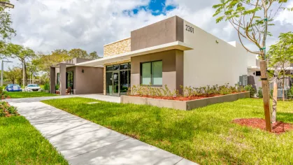 Exterior view of the Oak Enclave clubhouse, a sleek modern building with large windows, surrounded by manicured lawns, vibrant landscaping, and a welcoming entrance.