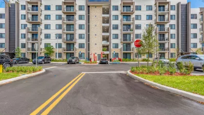 Front entrance of Oak Enclave Luxury Apartments, showcasing a five-story modern apartment building with ample parking, stylish balconies, and contemporary architectural design.