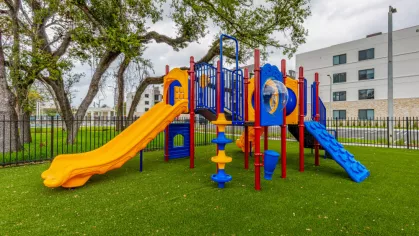 Vibrant outdoor playground at Oak Enclave Luxury Apartments, featuring colorful slides and climbing structures, surrounded by lush greenery and mature trees.