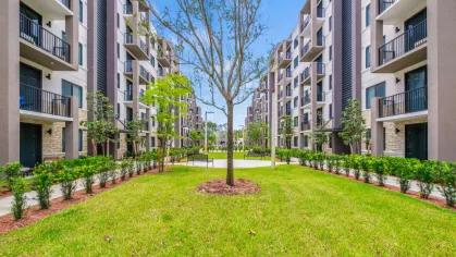 An inviting community park within Oak Enclave, lined with elegant apartment buildings, neatly trimmed hedges, and park benches for relaxation.