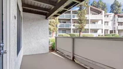 Private balcony with a covered ceiling, white stucco walls, and a view of surrounding apartment buildings.
