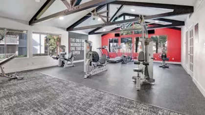 Modern fitness center with cardio and strength equipment, exposed beam ceiling, and bold red accent wall.