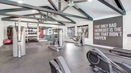 Spacious gym featuring exercise machines, free weights, and a motivational wall quote."