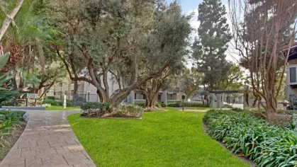 Lush green landscaping with mature trees and a winding pathway leading to apartment units.