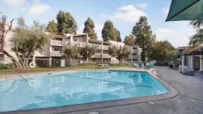 Outdoor swimming pool surrounded by lounge chairs and apartment buildings with balconies.